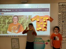 A couple grade one students at the front of the classroom wearing their orange shirts.