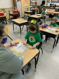 Grade two students dressed in their St. Patrick's gear, working at their desks.